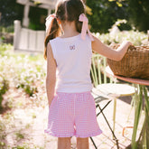 Back view of young girl in a garden wearing pink gingham Disney shorts for kids and a kids Disney tank top with a pink bow on the back.