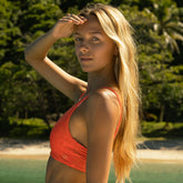 Close up of woman in an orange bikini top with the ocean and beach behind her