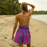 Back view of woman in a bold pink and blue bikini and cover-up shorts in a matching print on the beach.