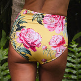Floral-patterned yellow swim bottoms with pink flowers and green leaves against a natural background.