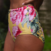 Floral-patterned yellow bikini bottom with pink flowers and green leaves on a blurred natural background.