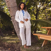 Woman in a white cotton cover-up set standing next to a palm tree in a tropical setting