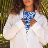 Close up of woman wearing a white flowy shirt over a blue floral swimsuit with palm leaves in the background