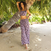 Woman in a floral outfit standing under a palm tree on a sandy path.