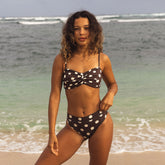 Woman in a polka dot bikini standing on a beach with ocean waves in the background