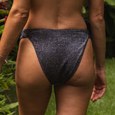 Person wearing dark glittery bikini bottoms outdoors with greenery in the background