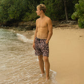 Man standing on a beach wearing patterned shorts with greenery in the background