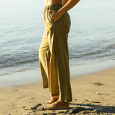 Woman wearing olive green cover-up pants standing on a beach with ocean in the background