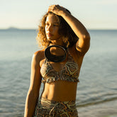 Woman in a neutral zebra print, ruffle bikini wearing goggles around her neck on the beach.