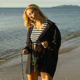 Woman on a beach wearing a black cover-up and striped bikini with an ocean in the background