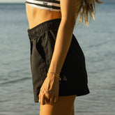 Woman wearing black linen shorts over a cute two-piece swimsuit by the water