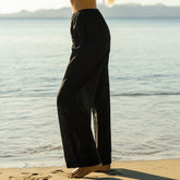 Woman wearing black linen pants standing on a beach with water in the background