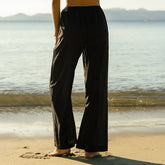 Woman wearing black wide-leg pants standing on a beach with ocean in the background