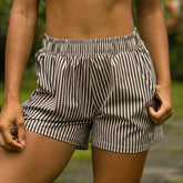 Close up of woman wearing brown striped boxer shorts as a swimsuit cover-up with a blurred background.