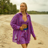 Woman in a pink and blue striped cover up outfit standing on a beach