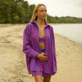 Woman wearing a pink and blue striped women's oversized button down top over a swimsuit on a beach