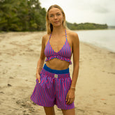 Woman wearing a pink and blue striped bikini top with trendy boxer shorts in blue and pink stripes on a beach.
