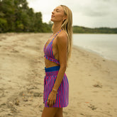 Woman in a colorful striped two piece swimsuit with matching boxer shorts standing on a beach.