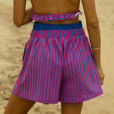 Back view of woman wearing a pink and blue striped bathing suit with matching trendy boxer shorts on a beach.
