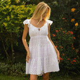 Woman wearing a white lace dress standing in a garden with greenery and flowers.