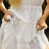 Close-up of a woman wearing a white eyelet dress with floral patterns, holding the hem.