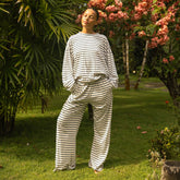 Woman wearing a navy blue and white striped lounge set standing in a garden with green grass and pink flowers.