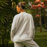Woman wearing a navy and white striped outfit standing in a garden with greenery and flowers.