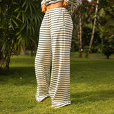 Woman wearing navy and white striped wide legged lounge pants standing on grass with a blurred natural background