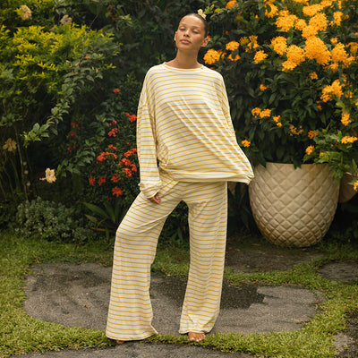 Woman in a yellow and white striped matching lounge set standing in a garden with flowers and plants.
