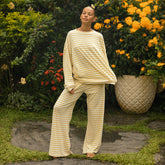Woman in a yellow and white striped pajama set standing in a garden with flowers and plants.