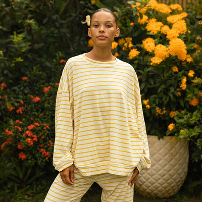 Woman wearing a yellow and white striped long sleeve tee with matching lounge pants standing in front of flowers