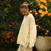 Side view of woman wearing a yellow and white striped shirt standing in front of flowers