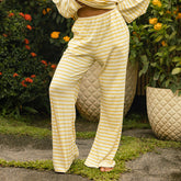 Woman wearing yellow and white striped casual pants standing outdoors with plants in the background
