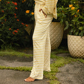 Woman wearing yellow and white striped pajama set standing outdoors with plants and flowers in the background.