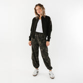 Model wearing women's black bomber jacket with cargo pants in camo print