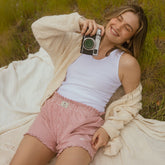 Model lying on a blanket holding a camera and wearing women's boxer shorts in red stripes with ruffle bottom detail.