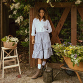 Model in a garden wearing a cute navy seersucker skirt that is a midi length skirt with a white button down and brown boots.