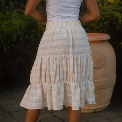 Back view of model wearing three tiered midi skirt in white lace-like cotton fabric.