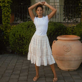 Model wearing white cotton skirt with three tiers. Made with lace-like fabric and hitting midi skirt length.