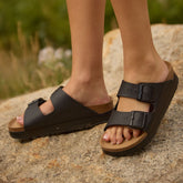 Black sandals with cork soles worn by a person on a stone surface with a natural background.
