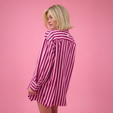 Back view of woman wearing pink striped button up shirt on a pink background