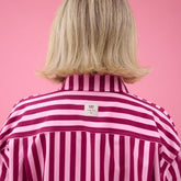Close up back view of woman wearing pink striped top with visible Albion logo tag on a pink background