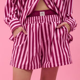 Woman wearing a pink striped women's boxer shorts with visible Albion logo tag and matching top in a studio with a pink background