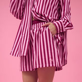 Woman in studio with pink background, wearing pink striped, cute women's boxer shorts and matching top.