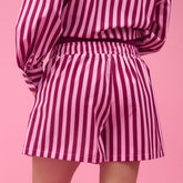 Back view of woman wearing pink striped shorts with a matching top on a pink background