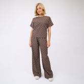 Woman wearing a brown polka dot matching set—brown polka dot flowy pants with matching top on a white background.