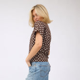 Side view of woman wearing a brown polka dot, elevated t-shirt and blue jeans on a white background