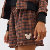 Close-up of brown Disney Mickey Lake Shorts showcasing plaid fabric, Mickey patch, and ruffled hem on a model