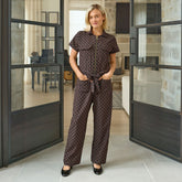 Woman wearing a brown polka dot, flattering women's jumpsuit standing in a modern interior setting.