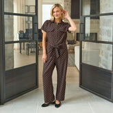Woman in a short-sleeved, polka dot jumpsuit standing in a modern interior setting with large glass doors.